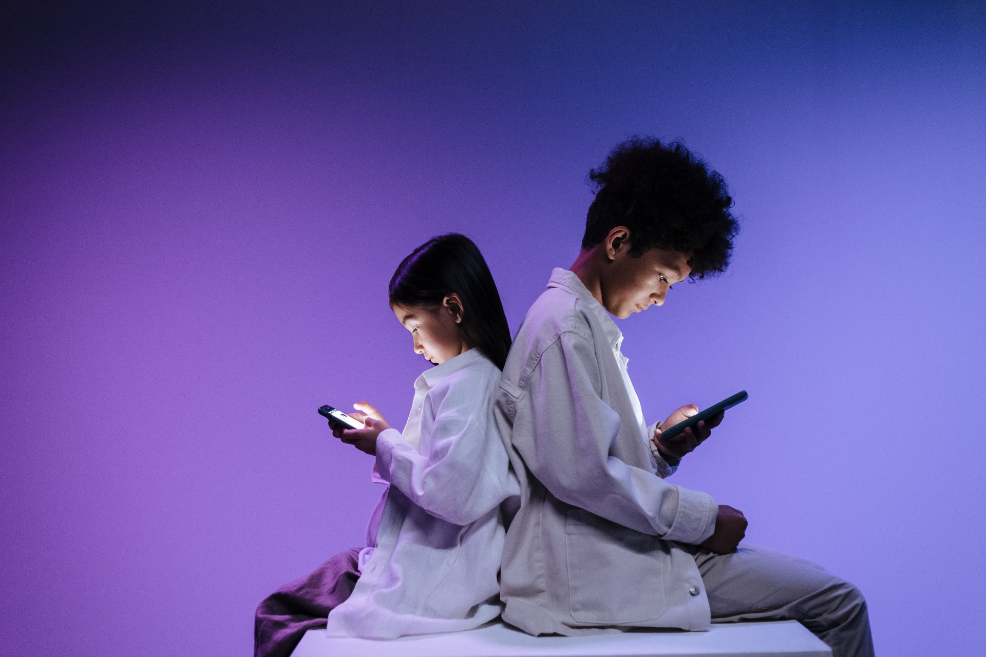 A boy and a girl sitting back to back, each absorbed in their smartphone screens